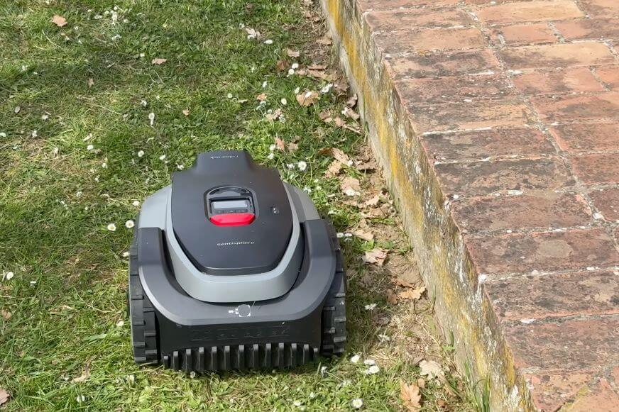 Roborock RockMow S1 mit Randschnittmodul fährt neben einem hohen Randstein und hinterlässt sichtbare ungemähte Streifen